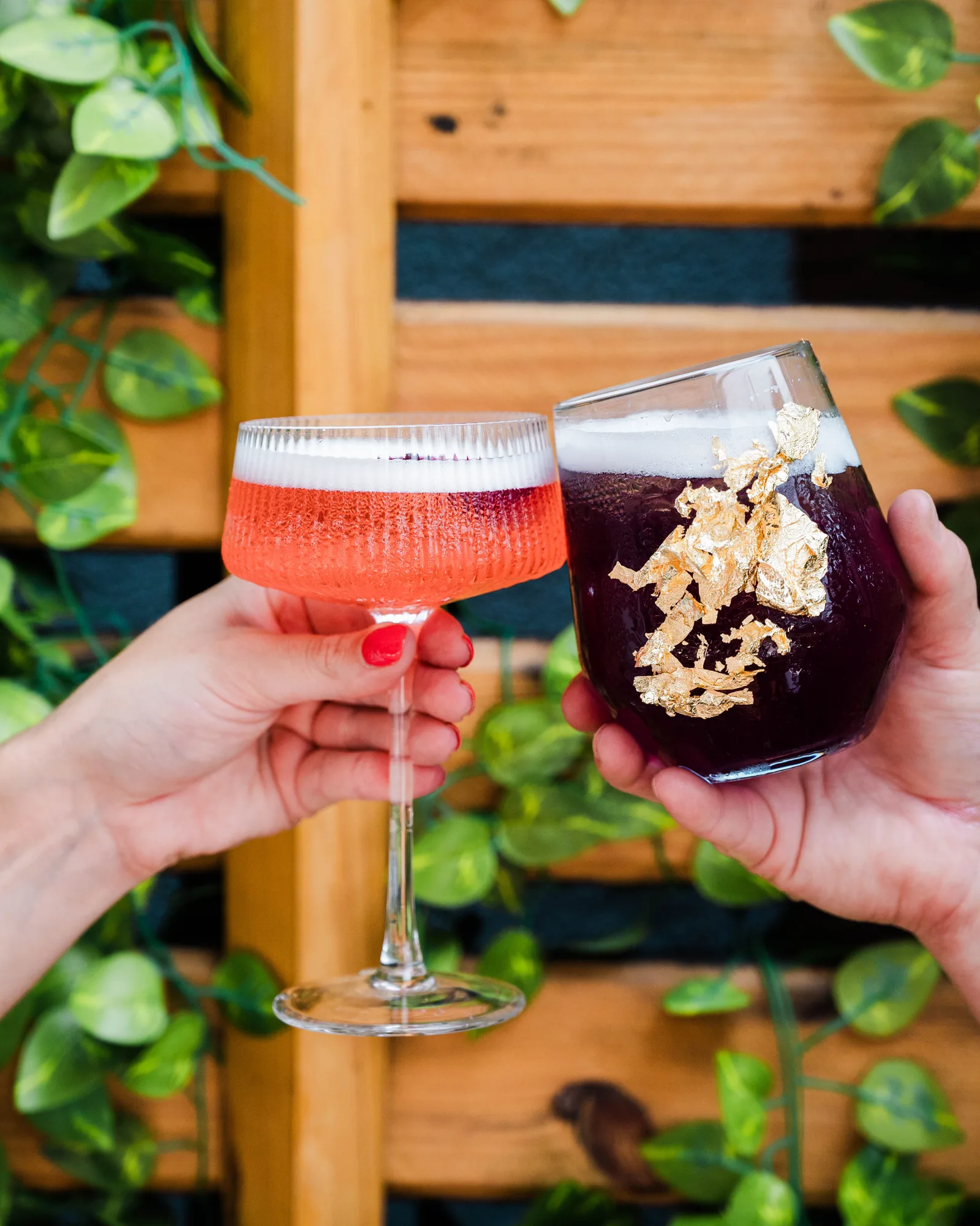 Two cocktails clinked against the trellis, one topped with gold leaf