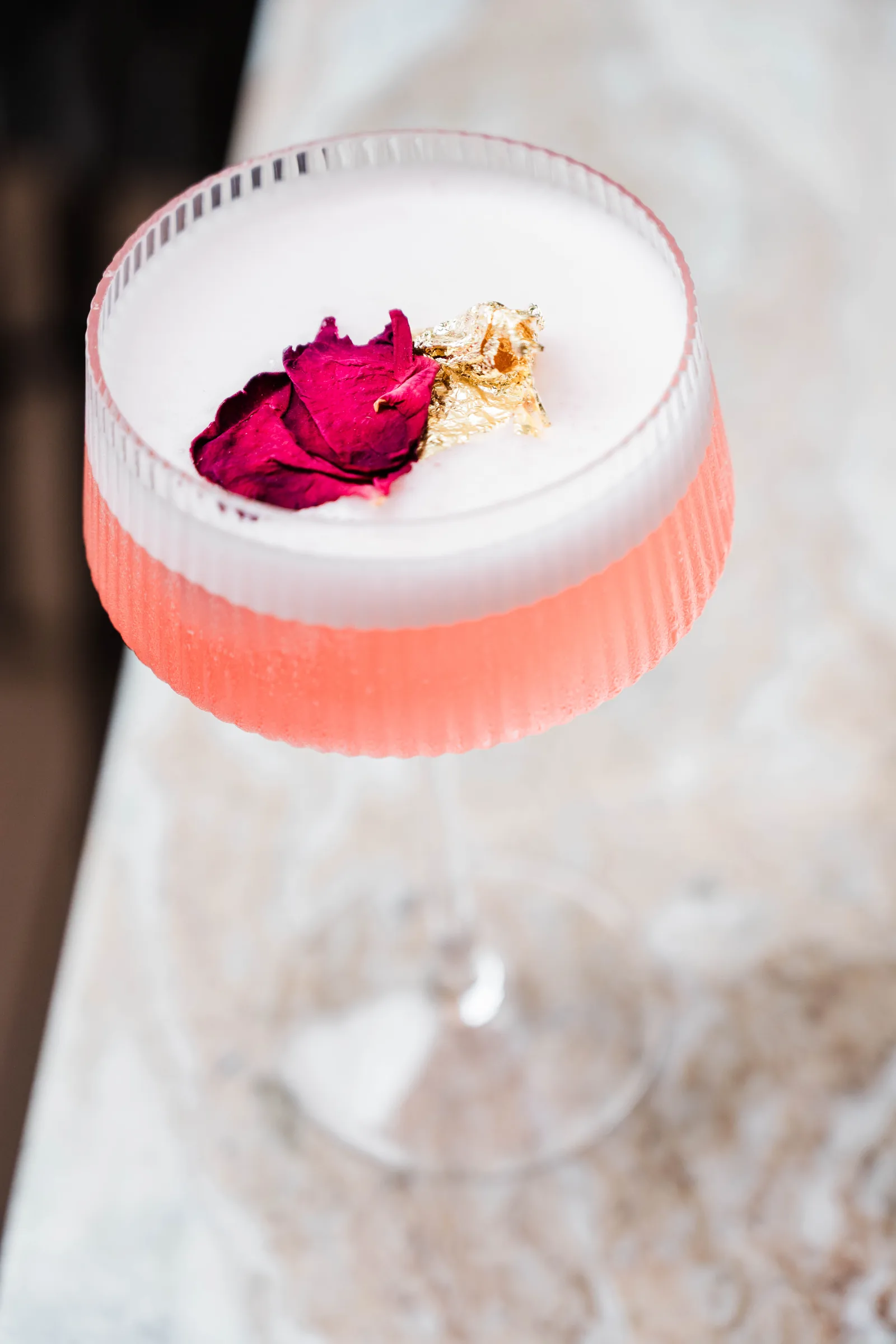 A rose petal and gold leaf on a pink coupe cocktail