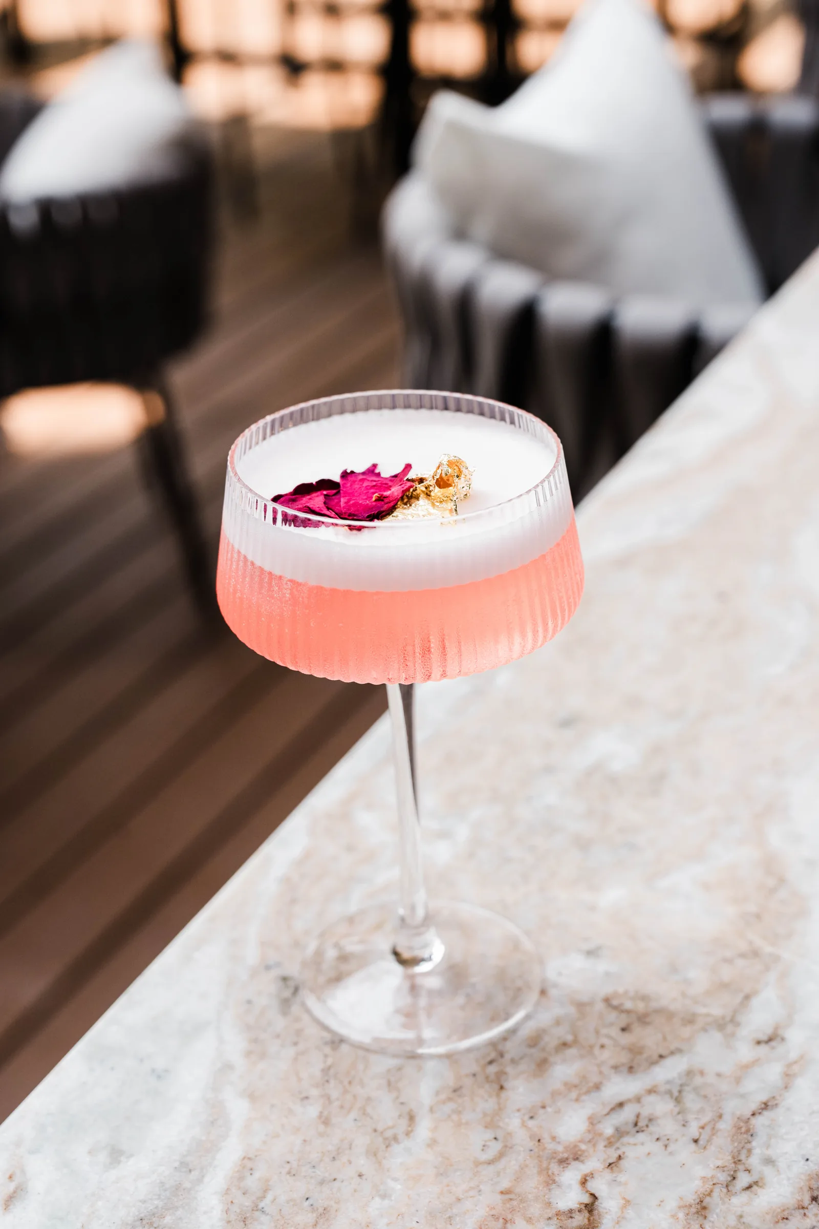 A pink coupe cocktail with a rose petal, set on the bar