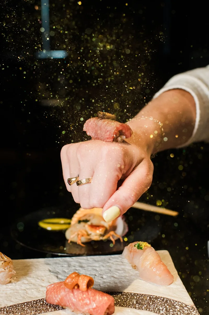 A chef finishing nigiri with gold dust at the Okane counter